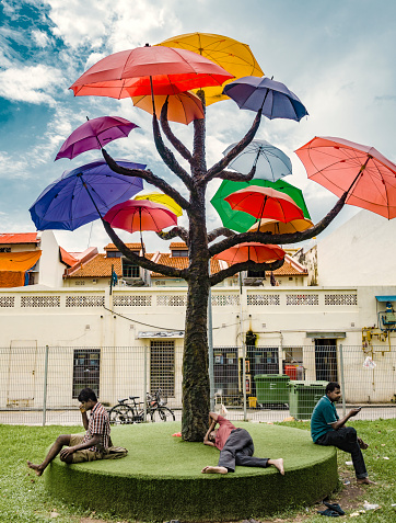 Group of men resting in a park with trees with umbrellas that provide shadow under the tropical heat of Singapore.. The art installation designed by Ms Marthalia Budiman is part of a new initiative in the city to bring artistic projects and performances to little India