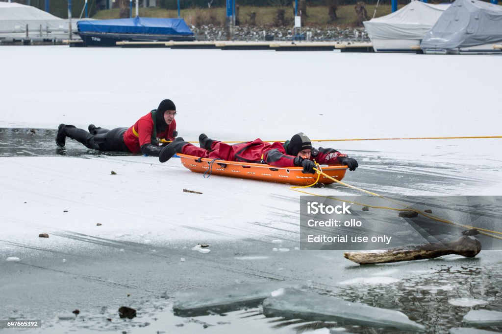 Ice rescue drill of DLRG at River Rhine - Einsatztaucher Wiesbaden, Germany - January 8, 2017: A fully equipped rescue diver and a lifeguard of German DLRG (Deutsche Lebensrettungsgesellschaft) during an ice rescue drill on ice-covered River Rhine at Schierstein harbor. The rescue teams practiced various possibilities to rescue persons who have broke through the ice and to search for persons with the help of divers under the ice layer. DLRG (Deutsche Lebensrettungsgesellschaft) is an independent NPO (nonprofit organization) based on volunteers. Adult Stock Photo