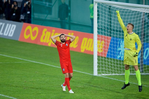 Football player holding head with disappointed while goalkeeper cheering around.