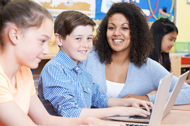 istock Teacher Helping Group Of Elementary School Children In Computer Class 647695404