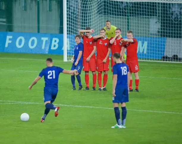 Football players defending in front of goal post during free kick.