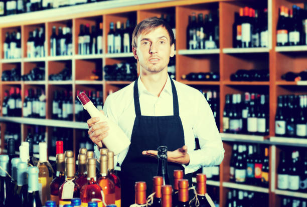 istock Man seller wearing uniform having bottle of wine 647703316
