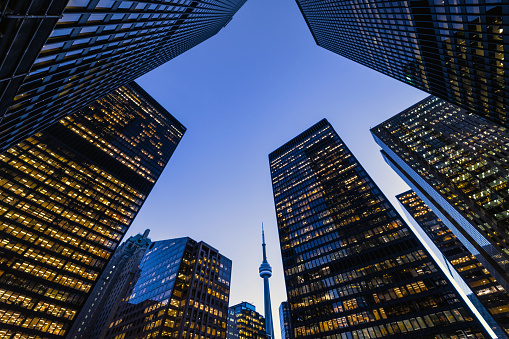 Business district architecture at night in downtown Toronto. Featuring a blue sky and lots of building lights with the famous CN Tower in the background.