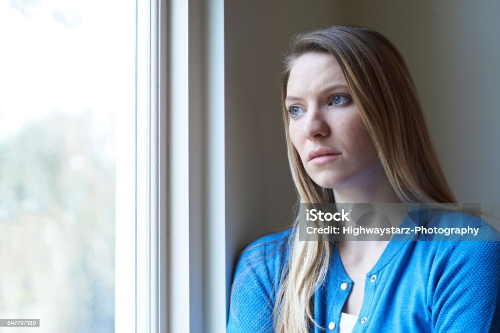 Mujer triste que sufre de depresión mirando por la ventana - Foto de stock de Preocupado libre de derechos