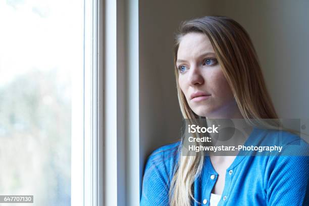 Mujer Triste Que Sufre De Depresión Mirando Por La Ventana Foto de stock y más banco de imágenes de Preocupado