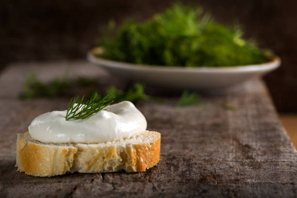 Fresh cream cheese on bread slice with dill on wooden background