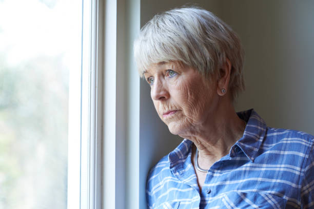 haute femme souffrant de dépression, regarde par la fenêtre - senior women depression sadness women photos et images de collection