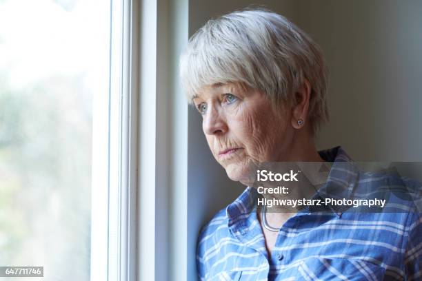 Senior Woman Suffering From Depression Looking Out Of Window Stock Photo - Download Image Now