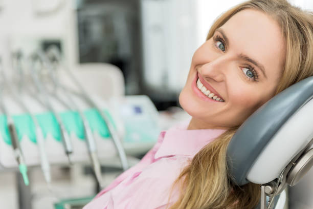 Attractive young woman visiting dentist Horizontal color image of attractive young woman waiting on dental exam, sitting on dentist's chair, sincerely smiling and looking at camera. Dental machinery at the background. dentists office photos stock pictures, royalty-free photos & images