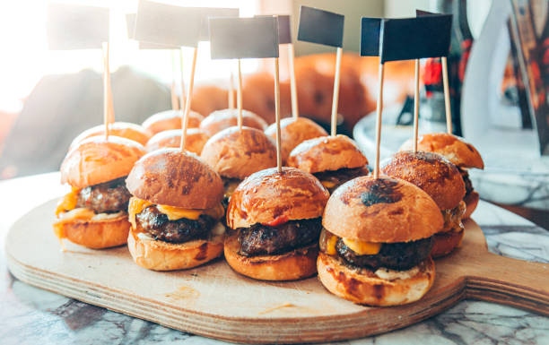Mini Hamburgers Assorted mini delicious cheeseburger sliders with cheese, onion and sauces with blank paper flag picks on wooden flag sliding stock pictures, royalty-free photos & images