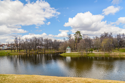 Spring view of the city park and pond, which reflects the blue sky with clouds