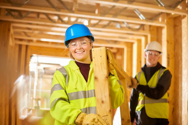 happy construction apprentices a female construction worker carries some studwork on a building site housing development and is assited by a male colleague . first job photos stock pictures, royalty-free photos & images