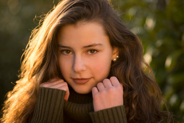 Teenage girl smiling at camera Outdoors portrait of a teenage girl with curly long brown hair in front of some leaves. She is looking friendly at the camera wearing a green pullover. jugendkultur stock pictures, royalty-free photos & images