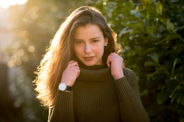 Teenage girl smiling at camera Outdoors portrait of a teenage girl with curly long brown hair in front of some leaves. She is looking friendly at the camera wearing a green pullover. jugendkultur stock pictures, royalty-free photos & images