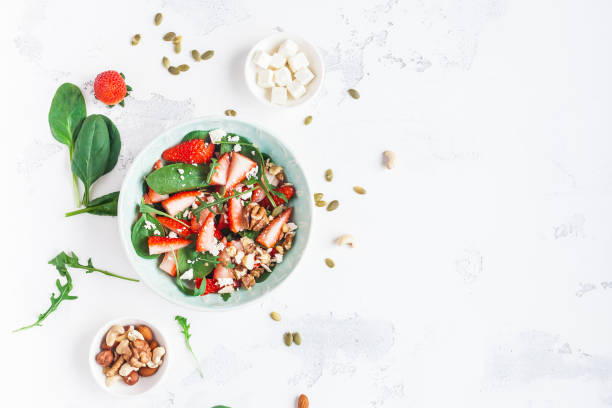 istock Spinach leaves, sliced strawberries, nuts, feta cheese on white background 647765938