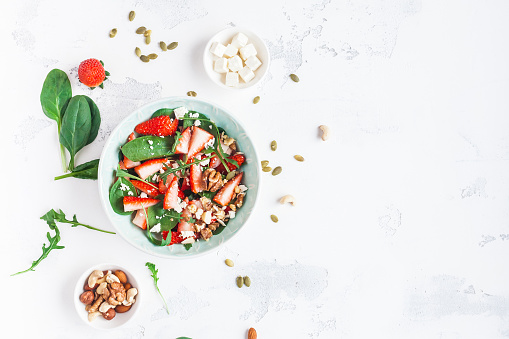 Spinach leaves, sliced strawberries, nuts, feta cheese on white background