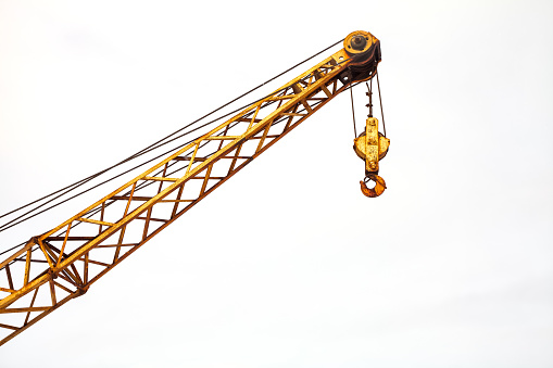 Yellow old rusty industrial construction crane with hook over cloudy sky