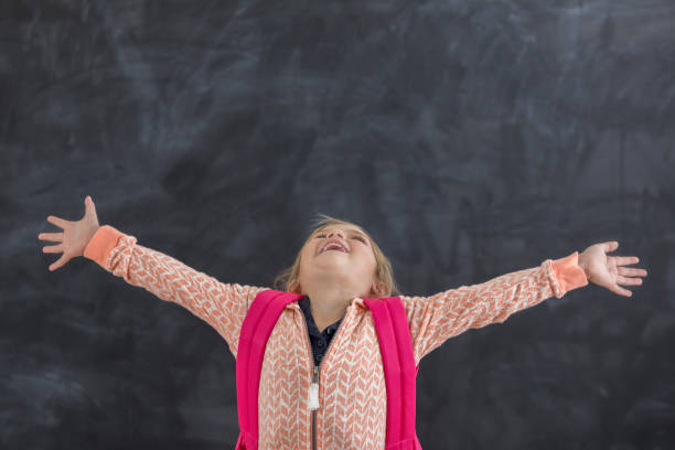 istock Joyful kindergarten student raises arms in classroom 647798742