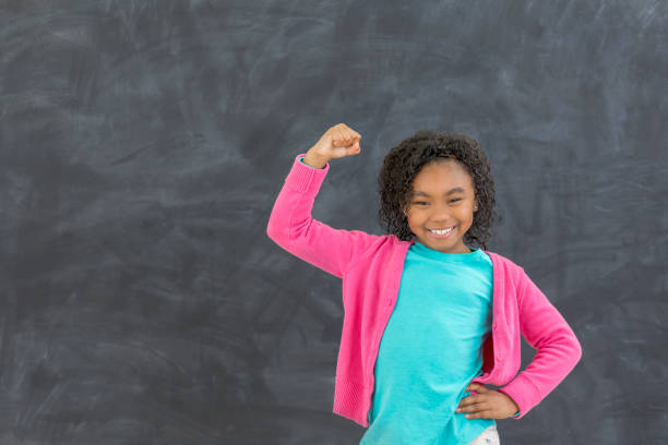 junges mädchen zeigt ihre muskeln in einem klassenzimmer - flexing muscles stock-fotos und bilder