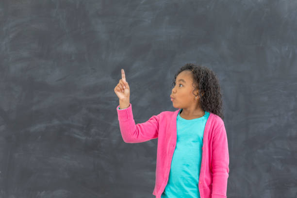 istock Pretty schoolgirl makes a face while looking at chalkboard 647799072