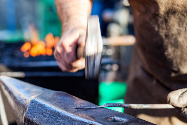 istock Blacksmith hammering iron rod on anvil in background fire 647801784