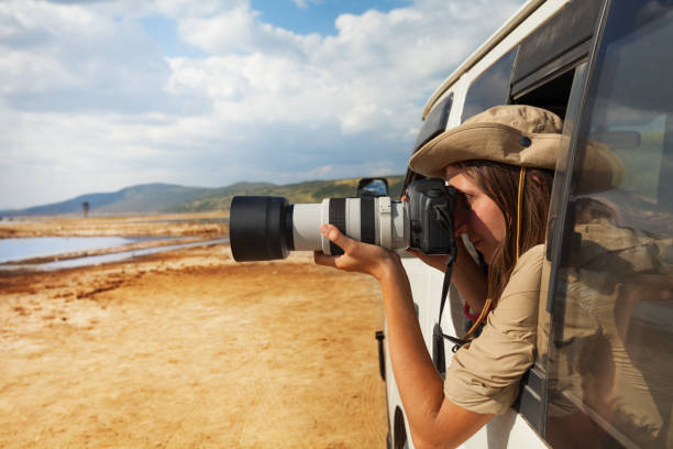 Girl taking photo of African savannah from jeep Side view portrait of young woman taking photo of Kenyan lake Nakuru from the open window of safari jeep maasai mara national reserve photos stock pictures, royalty-free photos & images