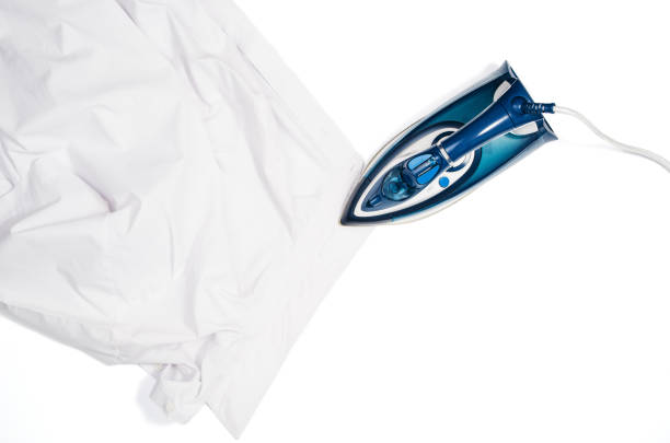 Female hand ironing clothes top view isolated on white background. Young woman with iron ironing man's shirt seen from above during housework. Blue iron on white table.