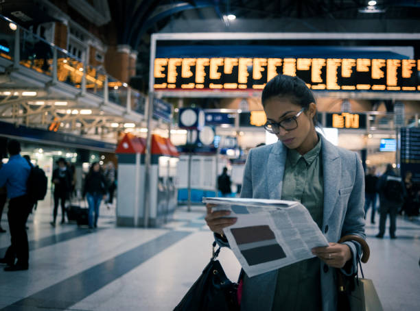 jeune femme lisant le journal à la station - traveling light photos et images de collection