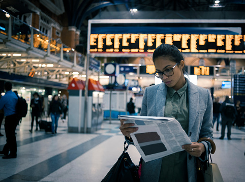 businesswoman reading newspaper while waiting for her train at the station