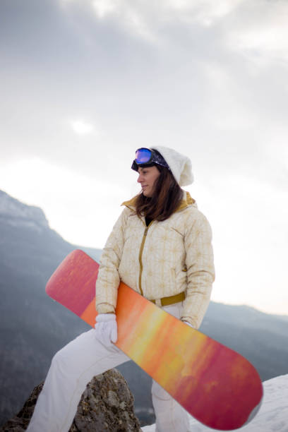 istock Woman holding snowboard with mountains in background 647979528
