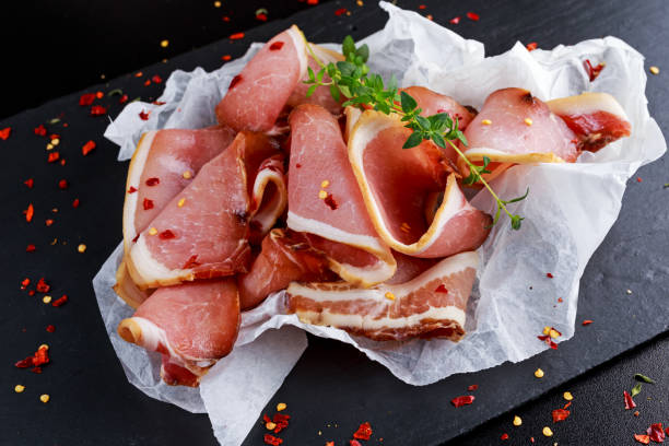 Raw beer bacon slices on crumpled paper which herbs Raw beer bacon slices on crumpled paper which herbs. uncooked bacon stock pictures, royalty-free photos & images