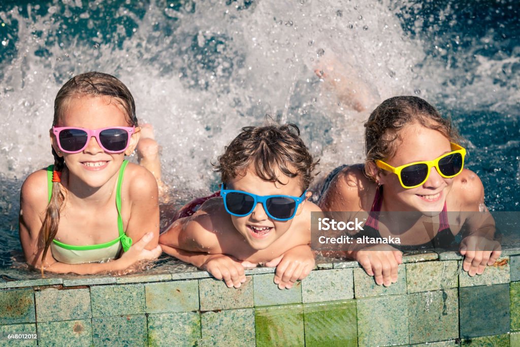 happy children  playing on the swimming pool at the day time. Three happy children  playing on the swimming pool at the day time. Concept of friendly family. Active Lifestyle Stock Photo