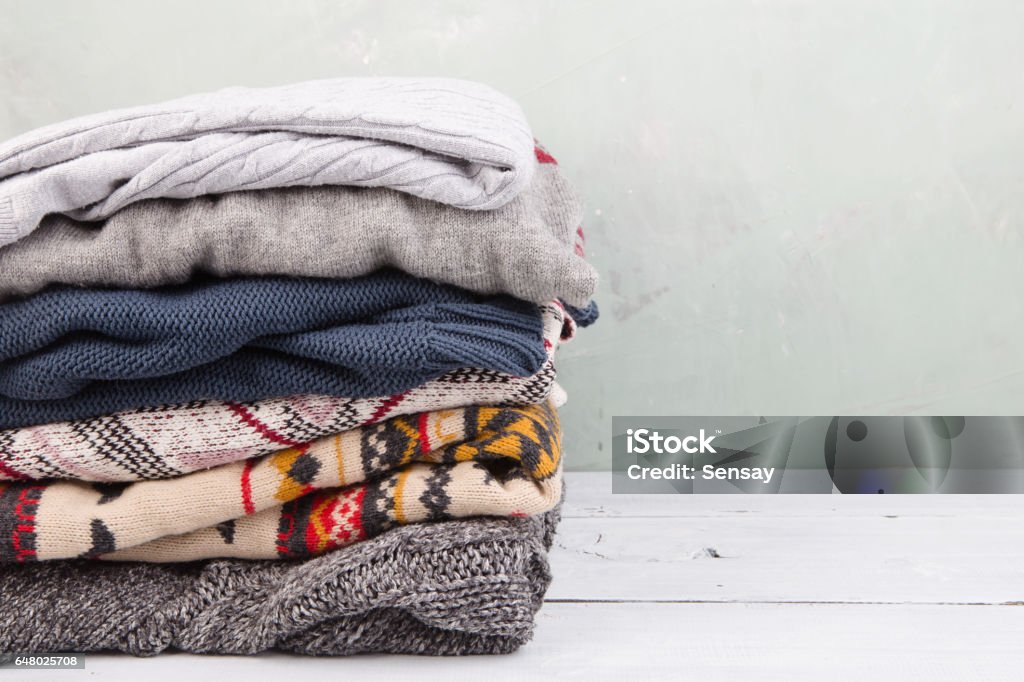 warm sweaters stacked on wooden table warm sweaters stacked on table Warm Clothing Stock Photo