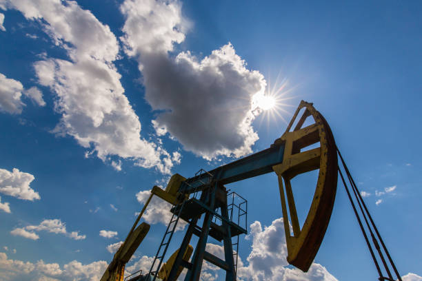 campo de petróleo com tomada de bomba, perfilado no céu azul com nuvens brancas, em um dia ensolarado - oil pump oil industry industry alberta - fotografias e filmes do acervo