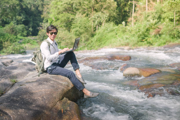 istock Businessman with backpack and laptop and phone at  waterfall  the forest. 648050830
