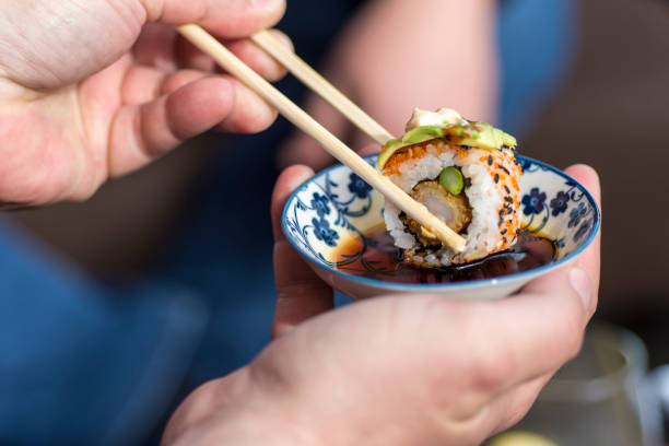 hand holding chopsticks to dip sushi roll in soy sauce - sushi food vegetarian food japanese cuisine imagens e fotografias de stock