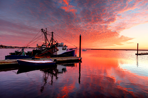 View along a wooden jetty in a harbor with docked ships in front of clouded sky in summer