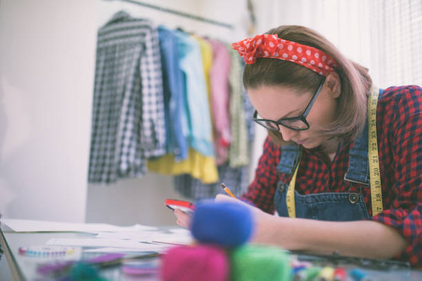 istock Young fashion designer talking on cellphone, watching her designs 648064690