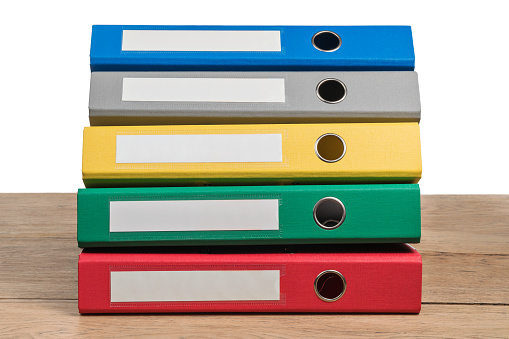 Several multi-colored office folders lying in a stack on a wooden table isolated on white background