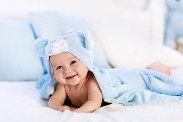 Baby in towel after bath in bed Baby boy wearing diaper and blue towel in white sunny bedroom. Newborn child relaxing in bed after bath or shower. Nursery for children. Textile and bedding for kids. New born kid with toy bear. towel photos stock pictures, royalty-free photos & images