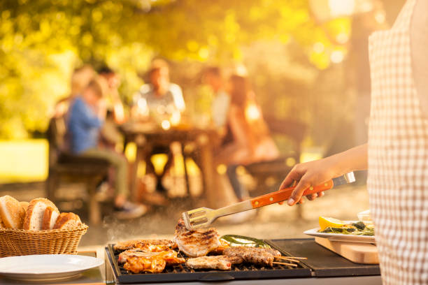 Preparing food for the family at picnic Rosting meat on barbecue for a family picnic in the back. Sun through the trees. grilled stock pictures, royalty-free photos & images