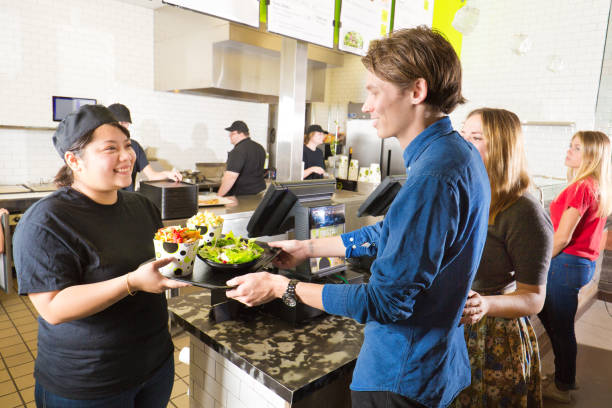 Kitchen and Wait Staff Serving Customers in Fast Food Restaurant Wait staff and kitchen staff working and serving customers over the counter in a fast food restaurant. fast food uniform stock pictures, royalty-free photos & images