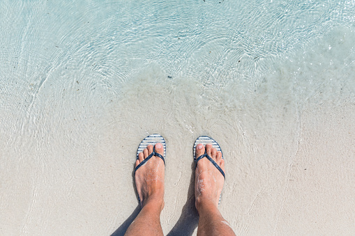 Male feet wearing female flip flops at beach. Funny image of a man at seaside trying to fit into woman footwear. Summer and travel concepts