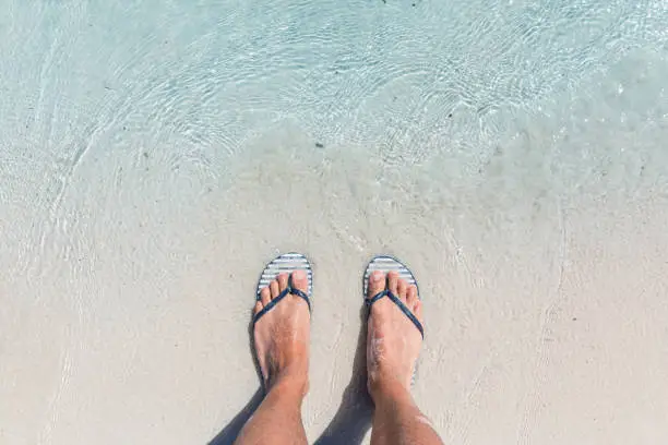 Photo of Male feet wearing female flip flops at beach