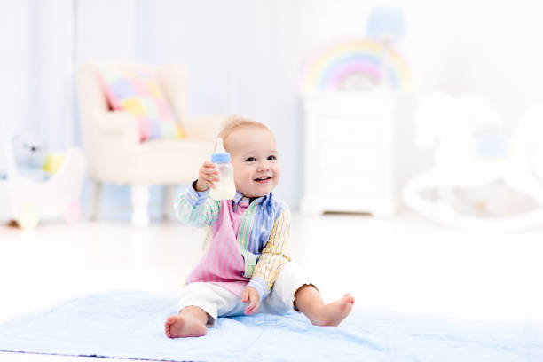 Little baby girl in white cotton bodysuit playing with teddy bear on carpet in living room