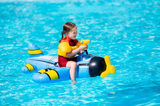 Little girl in swimming pool Little girl playing with inflatable toy airplane with water gun in outdoor swimming pool on hot summer day. Kids learn to swim. Children wearing sun protection rash guard relaxing in tropical resort baby gun stock pictures, royalty-free photos & images
