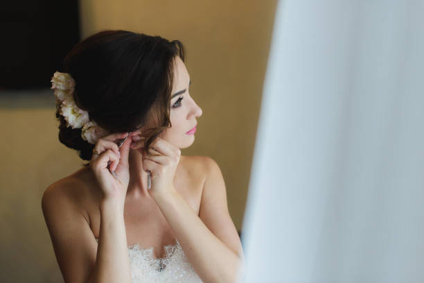 Bride in white wedding dress puts on earring.