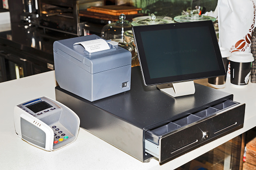 Point of sales computer terminal with touch screen tablet, cash register, mobile printer and card payment on a counter at a coffee shop.