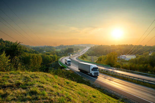 грузовики на шоссе обмотки через лесистый пейзаж на закате - truck horizontal shipping road стоковые фото и изображения