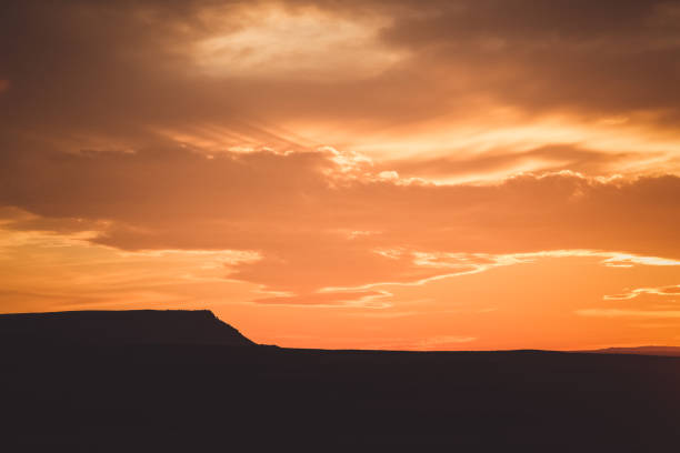Vibrant orange sunset and cloudy sky over a far away plateau and horizon in silhouette. Photo taken in Montana.